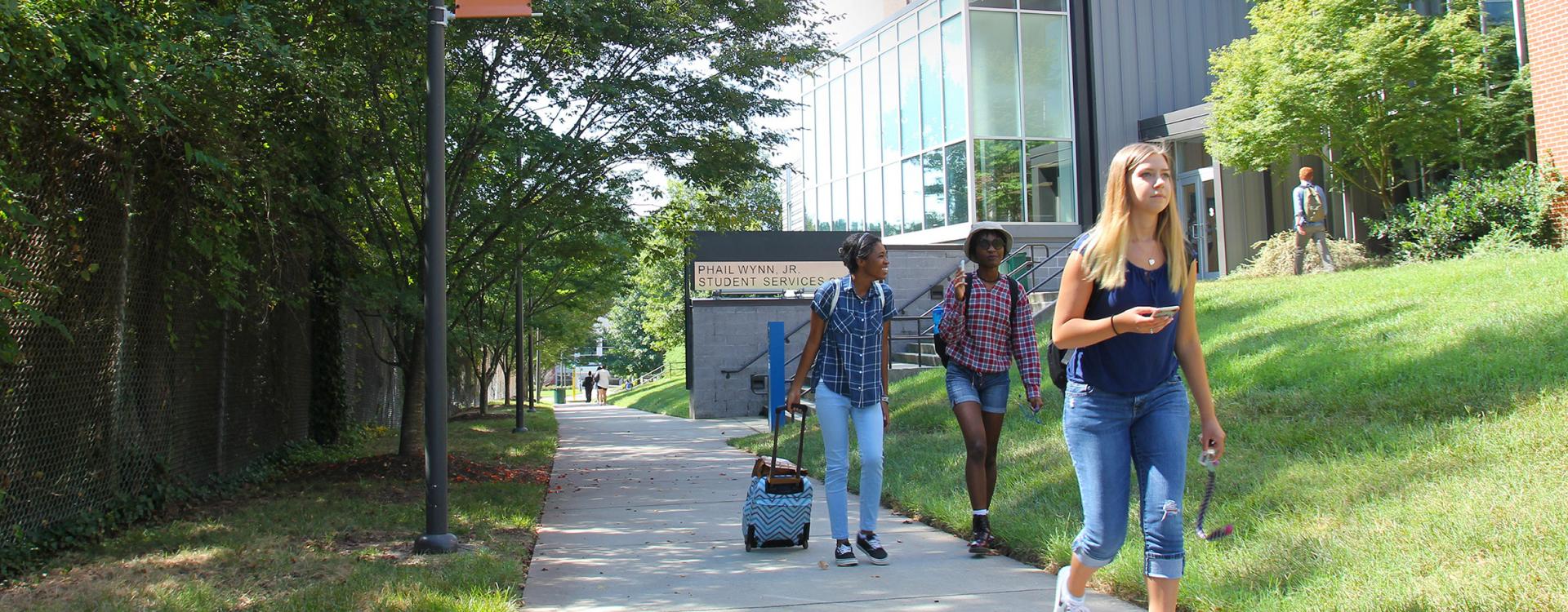 Three students walking on sidewalk in front of Wynn Center