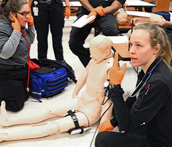 EMS instructors next to dummy talking to students in class